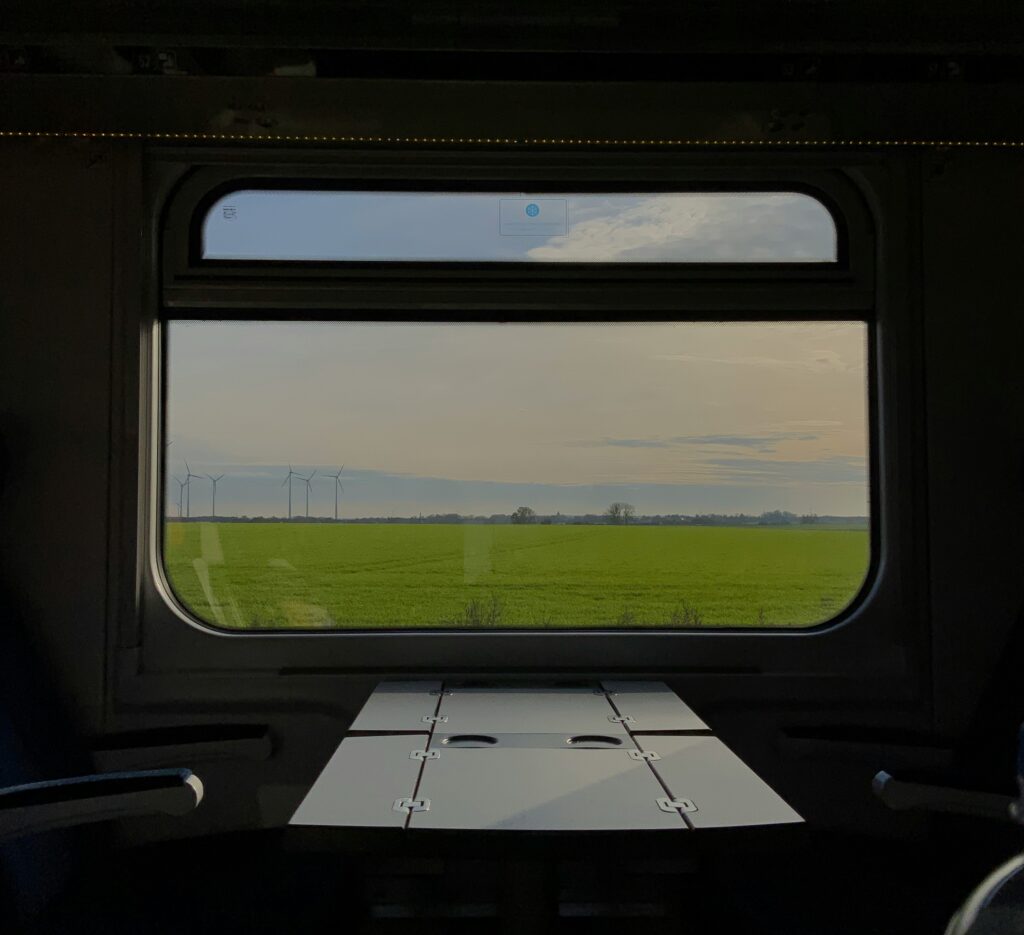 View from a train window looking out at a green field and open landscape ahead
